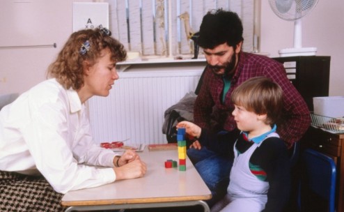 MODEL RELEASED. Child development: young boy (aged around 3-4 years) undertaking an intelligence test to estimate his reasoning skills. He is being asked to arrange the coloured blocks in accordance with instructions given by his assessor (left).